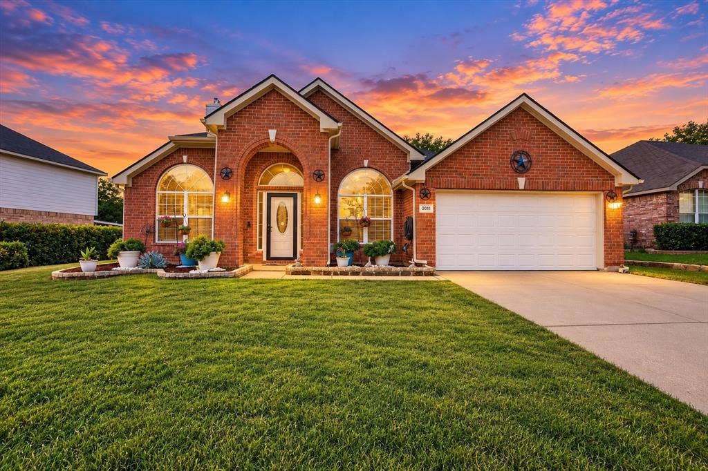 Brick exterior featuring an arched entryway, stone-bordered landscaping, arched windows, and an attached two-car garage