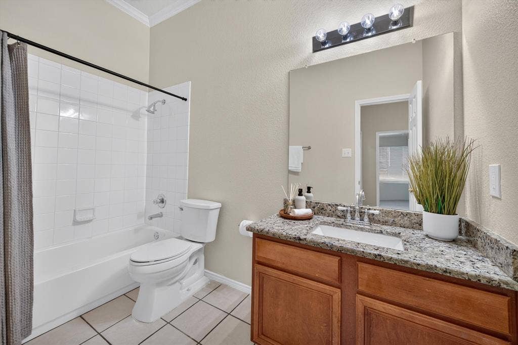 Bathroom featuring a wood vanity with a stone countertop, an integrated rectangular sink, a large wall-mounted mirror, and a tub-shower combination with tile surround