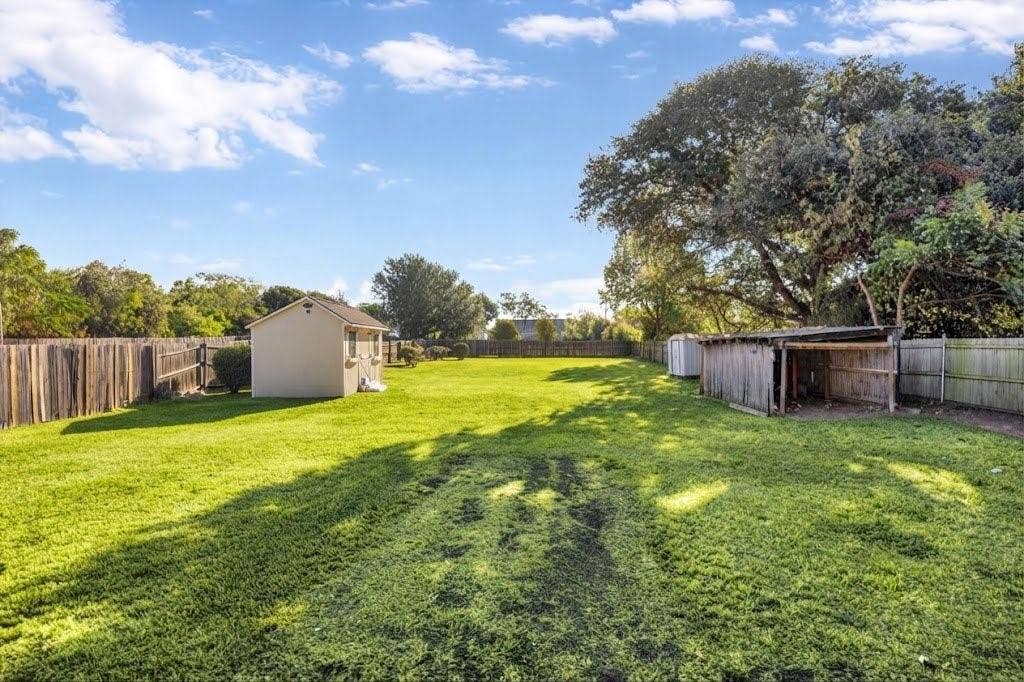 Expansive lawn featuring perimeter fencing, a freestanding shed, and mature trees