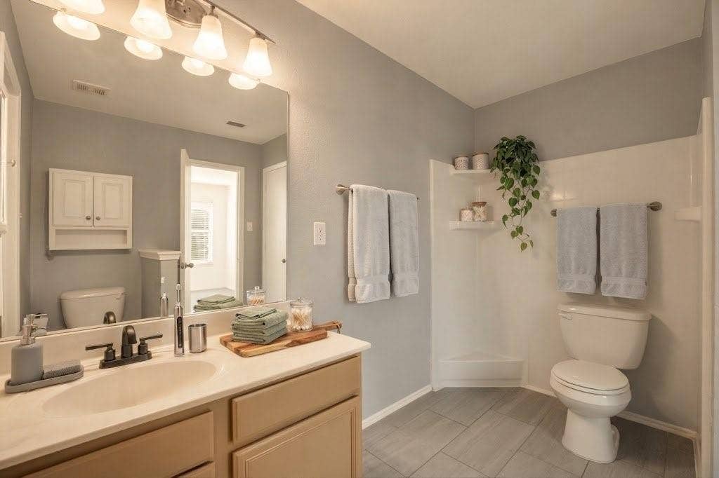 Bathroom featuring a vanity with an integrated sink, a single-handle faucet, a wall-mounted medicine cabinet, a toilet, and gray tile flooring