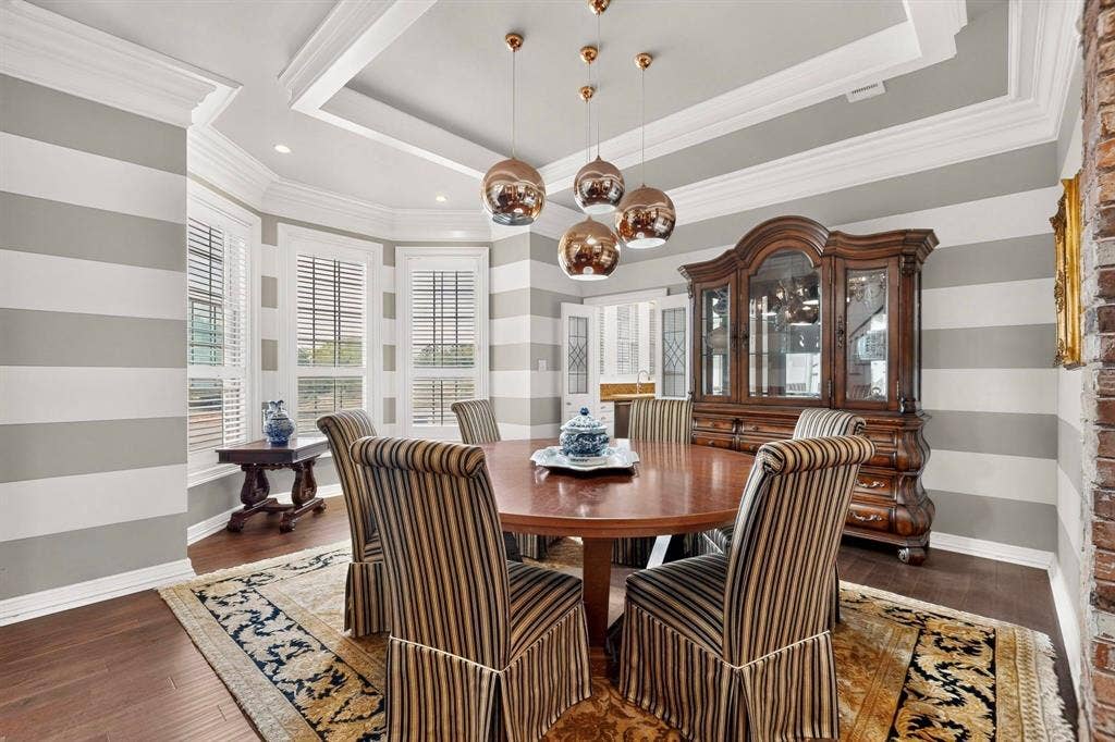 Dining area featuring a recessed tray ceiling, multi-light metallic pendant fixture, bay window configuration, and wood-finish flooring