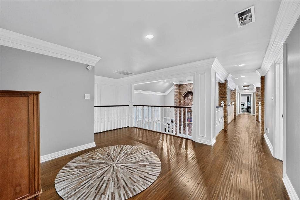 Interior area featuring wood-finish flooring, extensive crown molding, recessed lighting, white baluster railings, and exposed brick accents