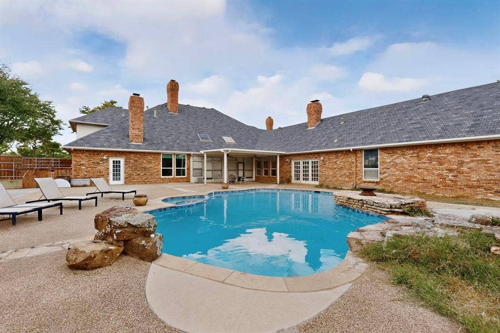 In-ground swimming pool with stone accents, brick exterior, multiple brick chimneys, concrete patio, and covered porch