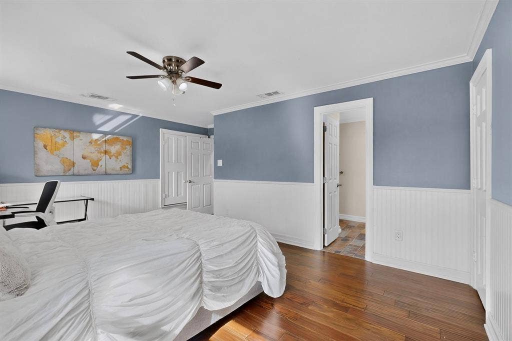 Room featuring wood-finish flooring, white beadboard wainscoting, multi-panel doors, and a ceiling fan with integrated light fixture