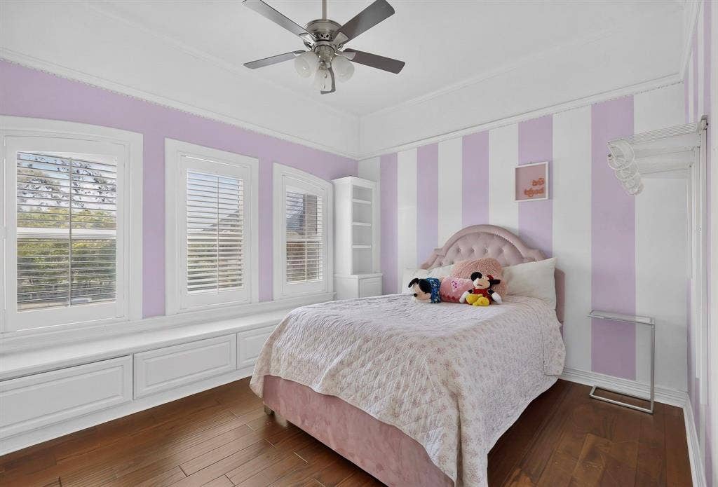 Wood-finish flooring, built-in window seating, plantation shutters, crown molding, and a ceiling fan with integrated lighting