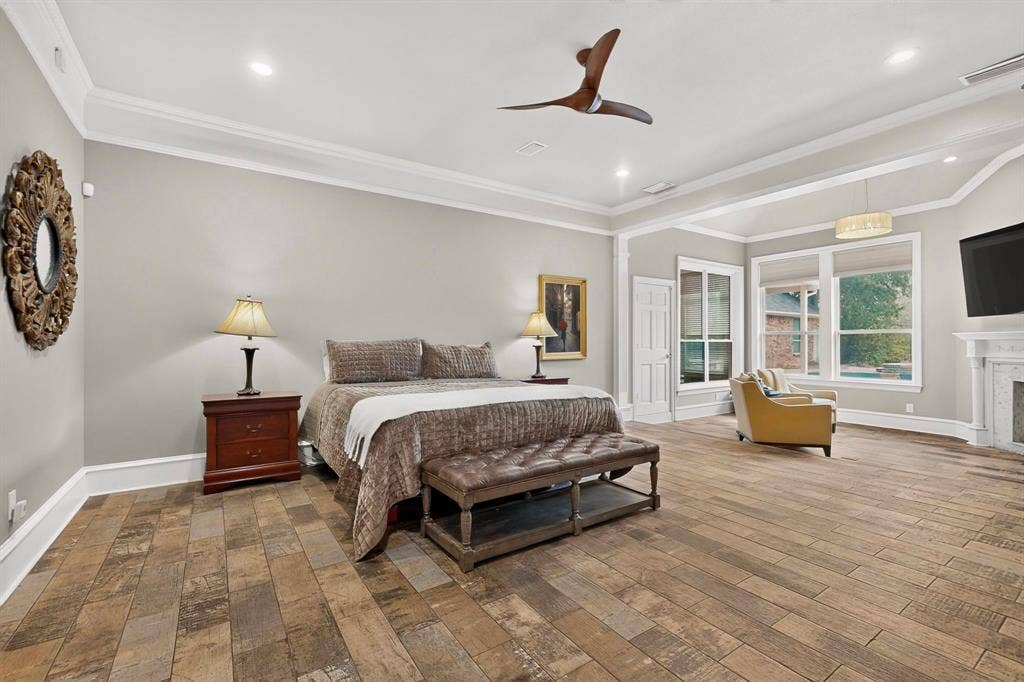 Spacious interior featuring wood-finish flooring, tray ceilings with crown molding, recessed lighting, a modern three-blade ceiling fan, and a fireplace with a traditional mantel