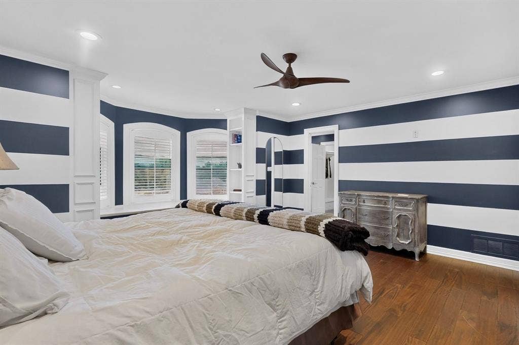Room featuring wood-finish flooring, recessed lighting, a modern ceiling fan, built-in shelving, and bay windows with plantation shutters