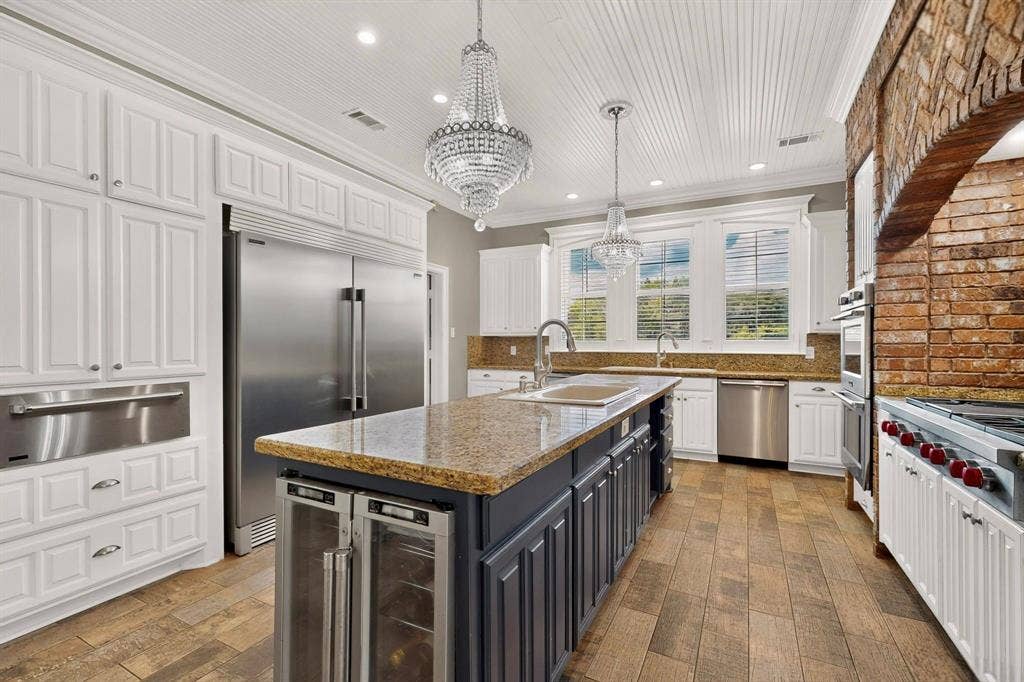 Kitchen featuring custom white cabinetry, a center island with built-in beverage refrigeration, stainless steel appliances, a brick-surround range alcove, and wood-finish flooring