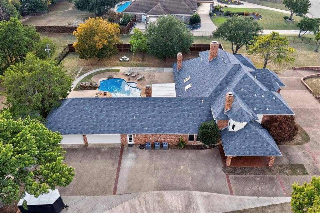 Aerial perspective of a multi-pitched roofline property featuring a brick exterior, in-ground swimming pool, masonry chimneys, and a multi-car garage