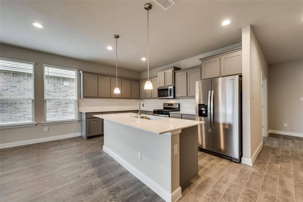 2441 Bellatrix Drive, Haslet, TX 76052 Kitchen featuring light hardwood / wood-style flooring, stainless steel appliances, sink, hanging light fixtures, and an island with sink