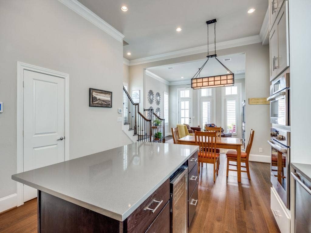 Kitchen island with a light-toned countertop, wood-finish flooring, built-in double oven, recessed lighting, and crown molding