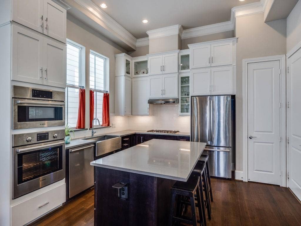 Stainless steel appliances, white shaker cabinetry, built-in double oven, deep farmhouse sink, and a contrasting island with seating