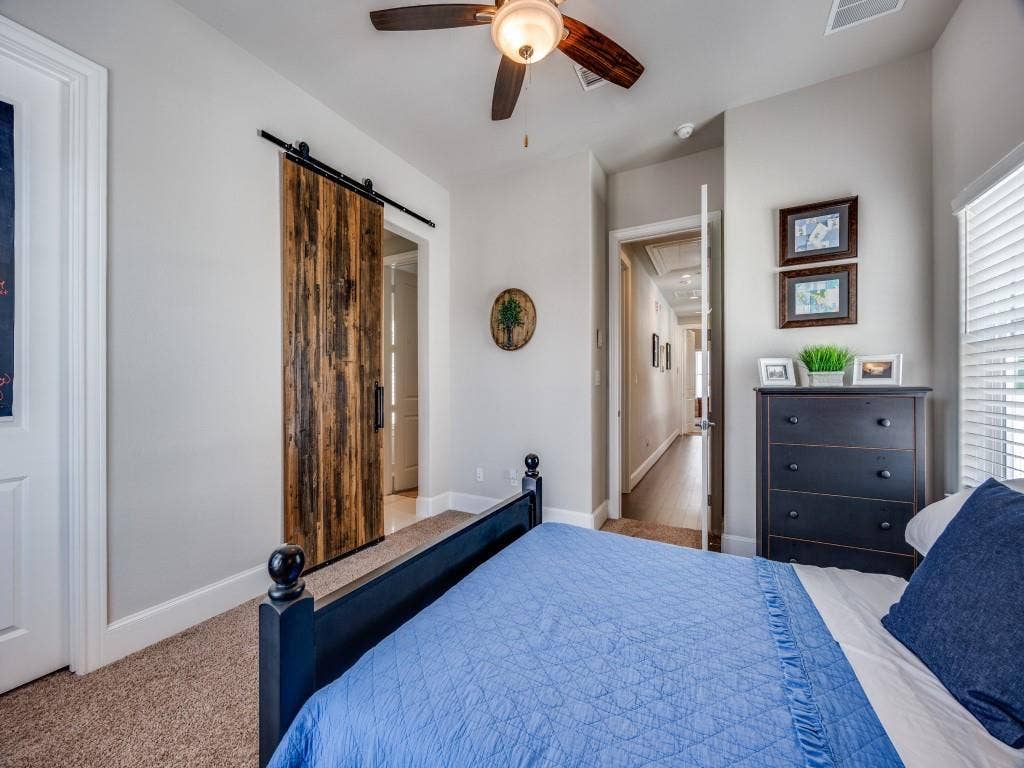 Barn door with black hardware, ceiling fan with integrated lighting, carpeted flooring, and window with blinds