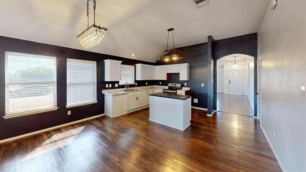 1815 Shanna Drive, Lancaster, TX 75134 Vaulted ceiling with a crystal chandelier, wood-finish flooring, white cabinetry, kitchen island with dark countertop, and an arched entry