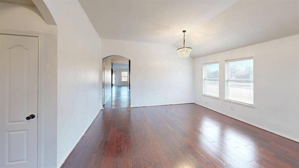 1815 Shanna Drive, Lancaster, TX 75134 Spacious room featuring wood-finish flooring, vaulted ceiling, dual windows with blinds, and a decorative chandelier