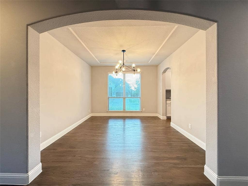 11818 Antler Drive, Frisco, TX 75035 Archway entry to a room featuring wood-finish flooring, a tray ceiling, and a modern chandelier