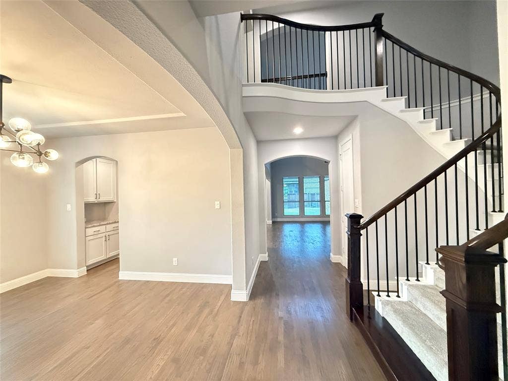 11818 Antler Drive, Frisco, TX 75035 Curved staircase with dark wood handrails and black metal balusters, tray ceiling with recessed lighting, wood-finish flooring, and arched doorways