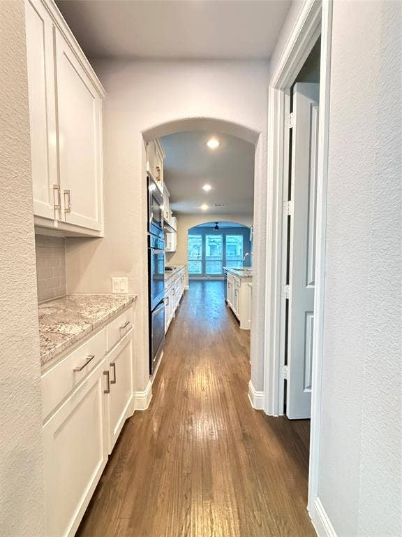 11818 Antler Drive, Frisco, TX 75035 White shaker cabinetry with brushed nickel hardware, light-toned granite countertops, wood-finish flooring, built-in double ovens, and an arched entryway