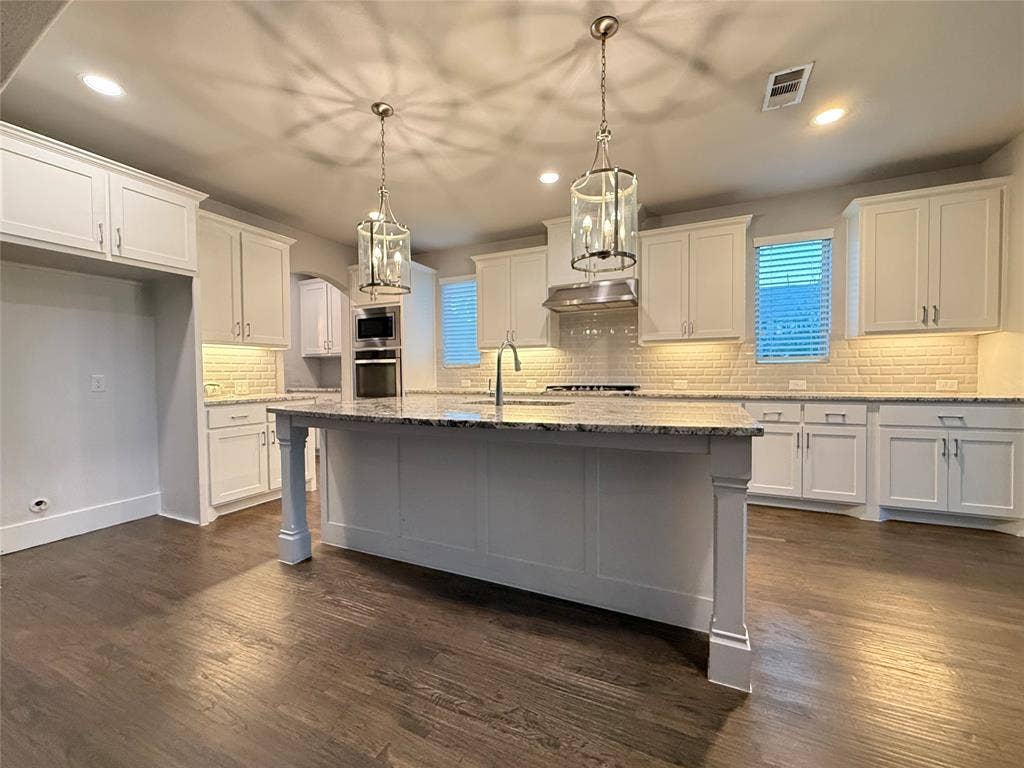 11818 Antler Drive, Frisco, TX 75035 Central island with stone countertop, wood-finish flooring, white cabinetry, integrated stainless steel appliances, and pendant lighting fixtures