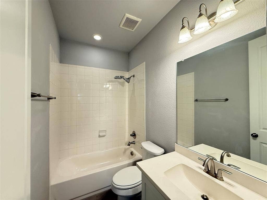 11818 Antler Drive, Frisco, TX 75035 White tile bath surround, recessed ceiling lighting, vanity with integrated sink, brushed nickel faucet, and vanity mirror