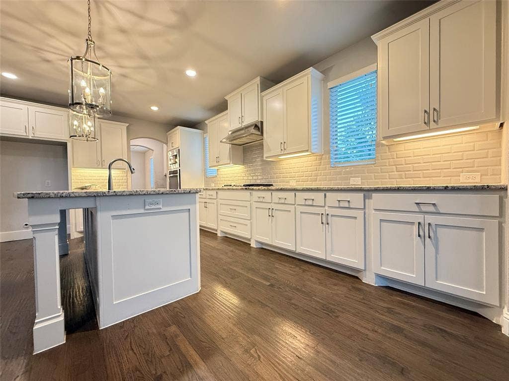 11818 Antler Drive, Frisco, TX 75035 White shaker cabinetry, wood-finish flooring, undermount sink, subway tile backsplash, and an island with a stone countertop