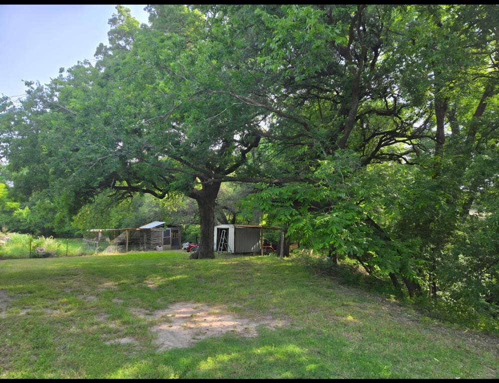 6220 W Highway 199, Springtown, TX 76082 Expansive lot featuring mature trees, a metal shed, and a fenced enclosure