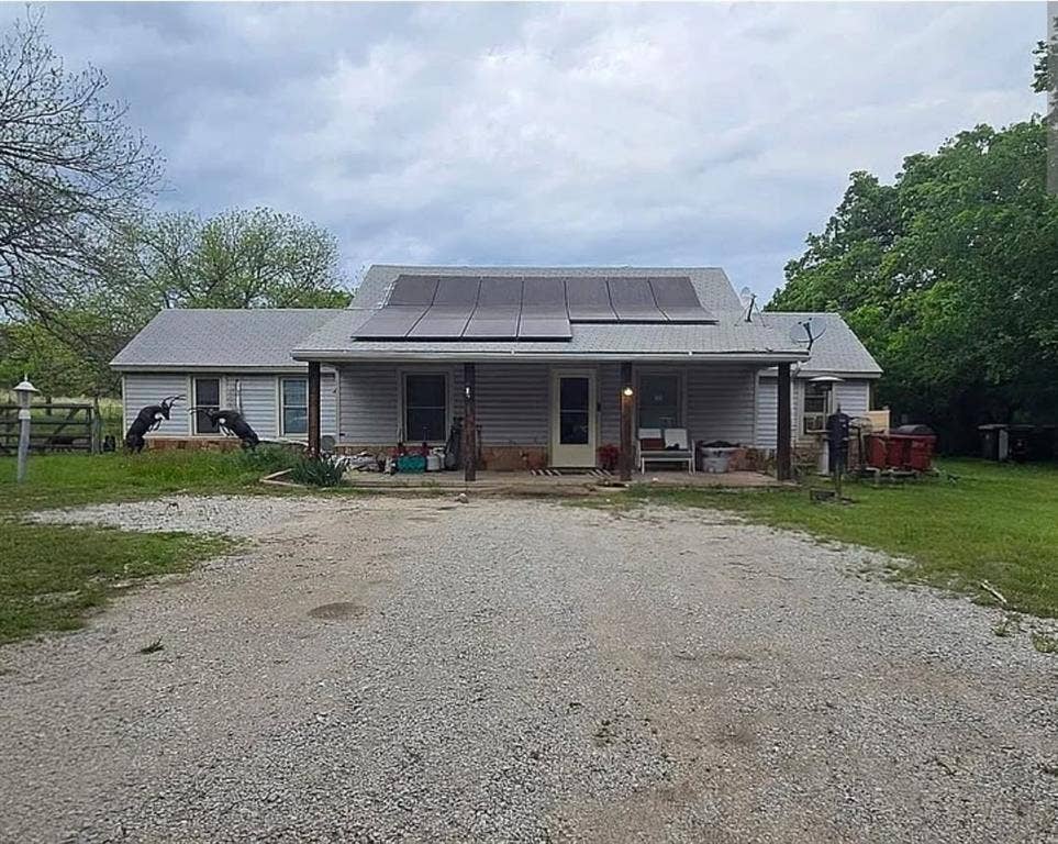 6220 W Highway 199, Springtown, TX 76082 Gable roof with integrated solar panels, covered front porch, horizontal siding, stone accent base, and gravel driveway