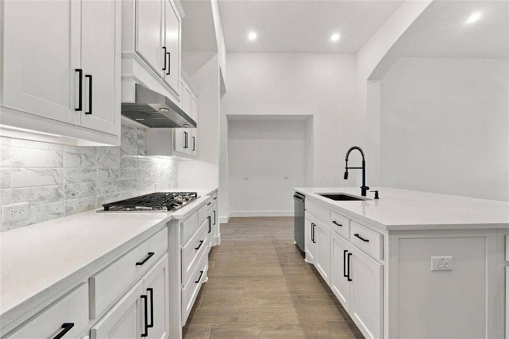 White shaker cabinetry, light-toned wood-finish flooring, white countertops, built-in gas range, and a black gooseneck faucet