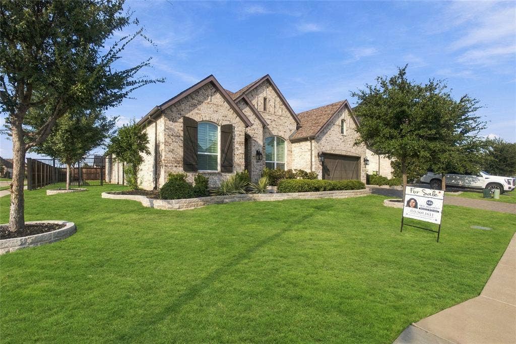 Arched windows with shutters, attached garage, and a manicured lawn with stone-edged landscaping