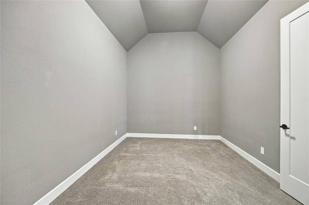 Vaulted ceiling, neutral wall paint, carpet flooring, white trim, and a contemporary door with matte black hardware