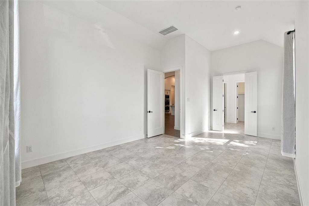 Spacious room featuring vaulted ceilings, recessed lighting, tile flooring, and multiple doorways with modern hardware