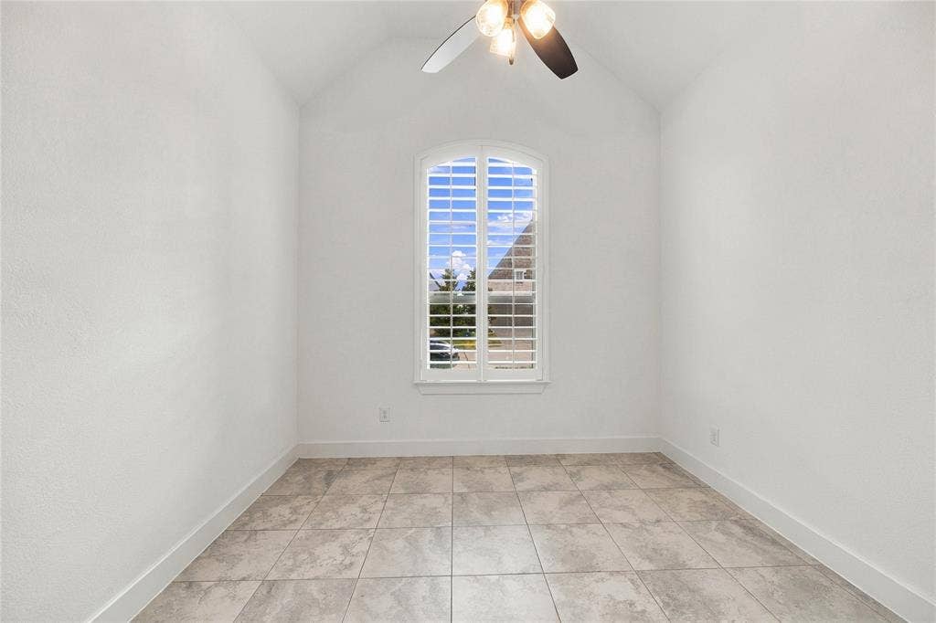 Vaulted ceiling with an attached ceiling fan, arched window with plantation shutters, and large format tile flooring, ensuite bath