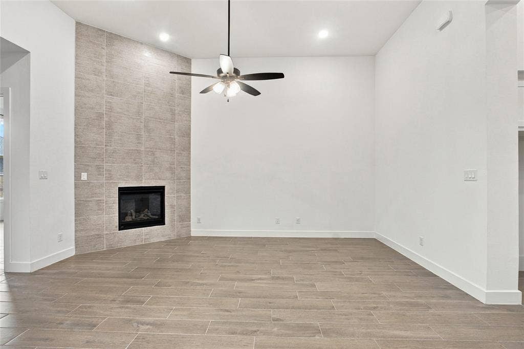 Floor-to-ceiling tile fireplace surround with a gas insert, wood-finish flooring, recessed lighting, and a ceiling fan