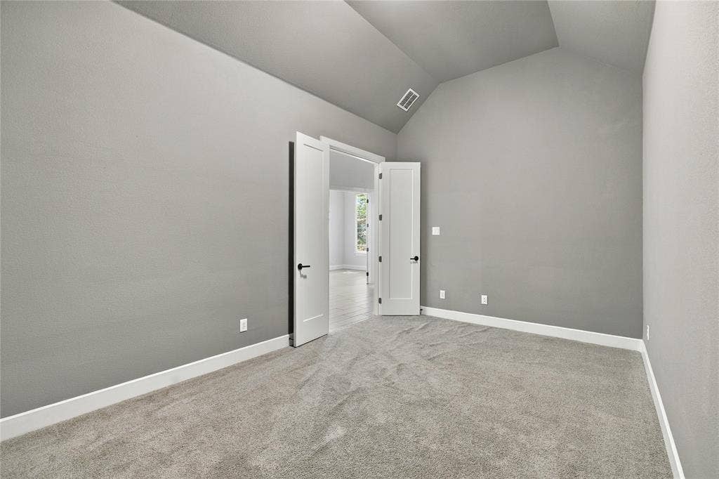 Vaulted ceiling, gray carpeting, neutral wall finishes, and white interior doors with dark hardware