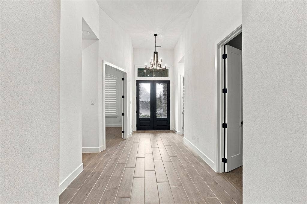 Vaulted entry with wood-look tile flooring, a black double-door entry, a transom window, and a chandelier