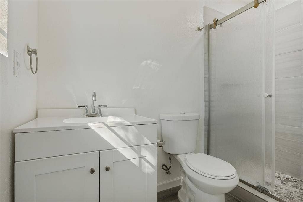 1522 Carroll Drive, Garland, TX 75041 White shaker-style vanity with a solid-surface countertop, under-mount sink, chrome faucet, and walk-in shower with a sliding glass door