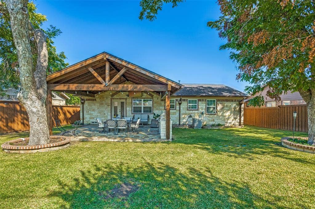 1522 Carroll Drive, Garland, TX 75041 Backyard featuring a stone-clad exterior, covered patio with exposed wood beams, flagstone flooring, and brick-rimmed mature tree planters