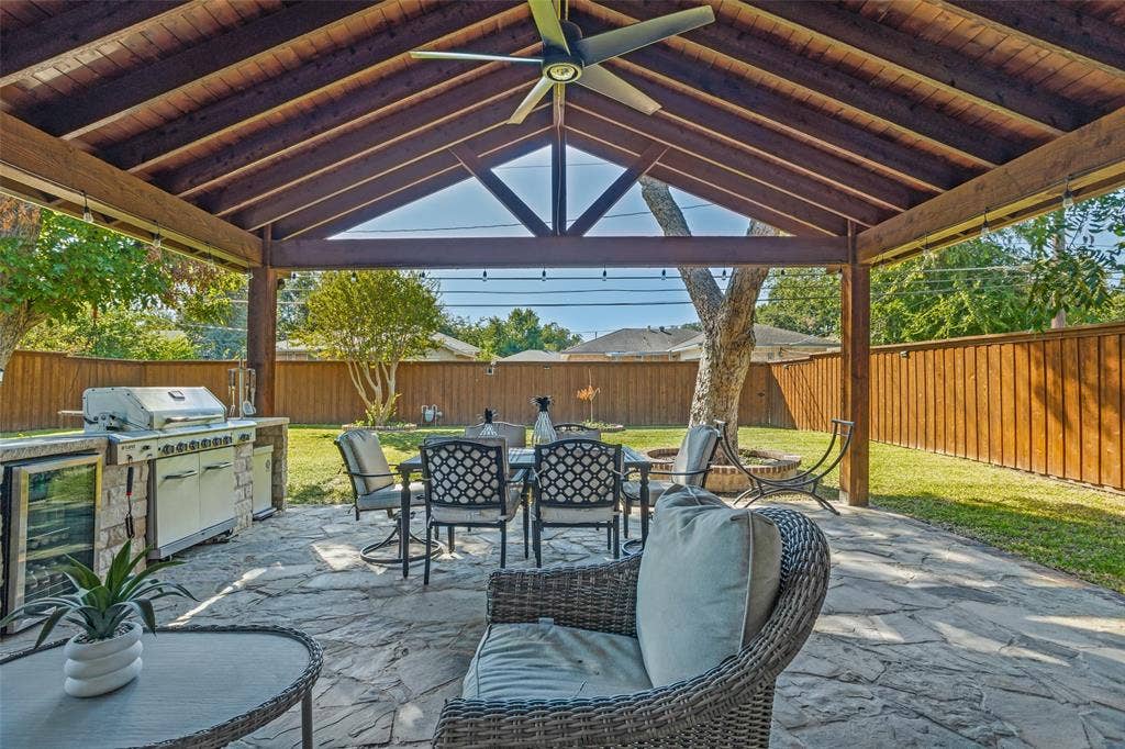 1522 Carroll Drive, Garland, TX 75041 Covered patio featuring an exposed timber-beam ceiling, stone-paved flooring, built-in outdoor kitchen with stone base, and a dedicated ceiling fan