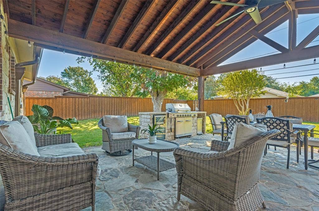 1522 Carroll Drive, Garland, TX 75041 Covered patio featuring an exposed timber-beam vaulted ceiling, a built-in outdoor kitchen with stone masonry, a stainless steel grill, and irregular flagstone paving