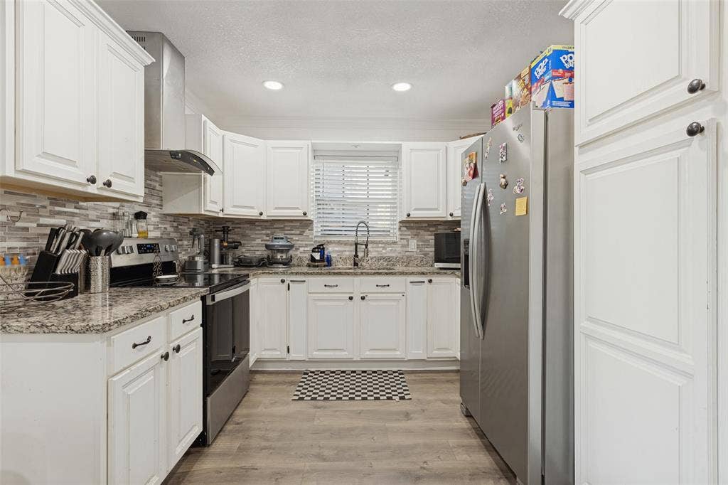 1522 Carroll Drive, Garland, TX 75041 Kitchen featuring white shaker-style cabinetry, stone-finish countertops, stainless steel appliances, a multi-tonal linear tile backsplash, and wood-finish flooring