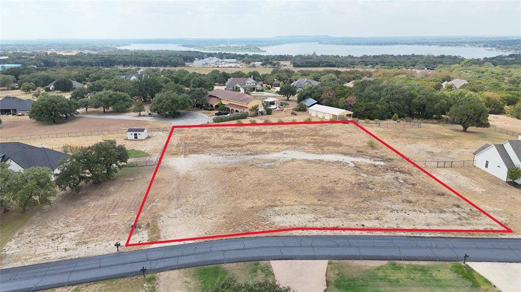 157 Helton Drive, Granbury, TX 76049 Undeveloped land parcel with a paved road frontage, surrounded by established properties and distant water scenery