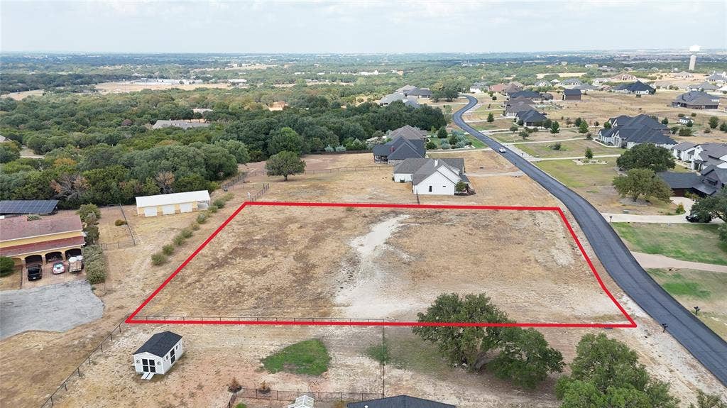 157 Helton Drive, Granbury, TX 76049 Expansive undeveloped lot with a level grade, surrounded by mature trees and residential properties, featuring direct access to a paved road