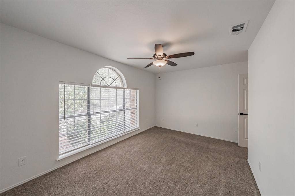 617 Dover Court, Coppell, TX 75019 Arched transom window above a large rectangular window, textured carpeting, neutral wall paint, and a ceiling fan with light fixture