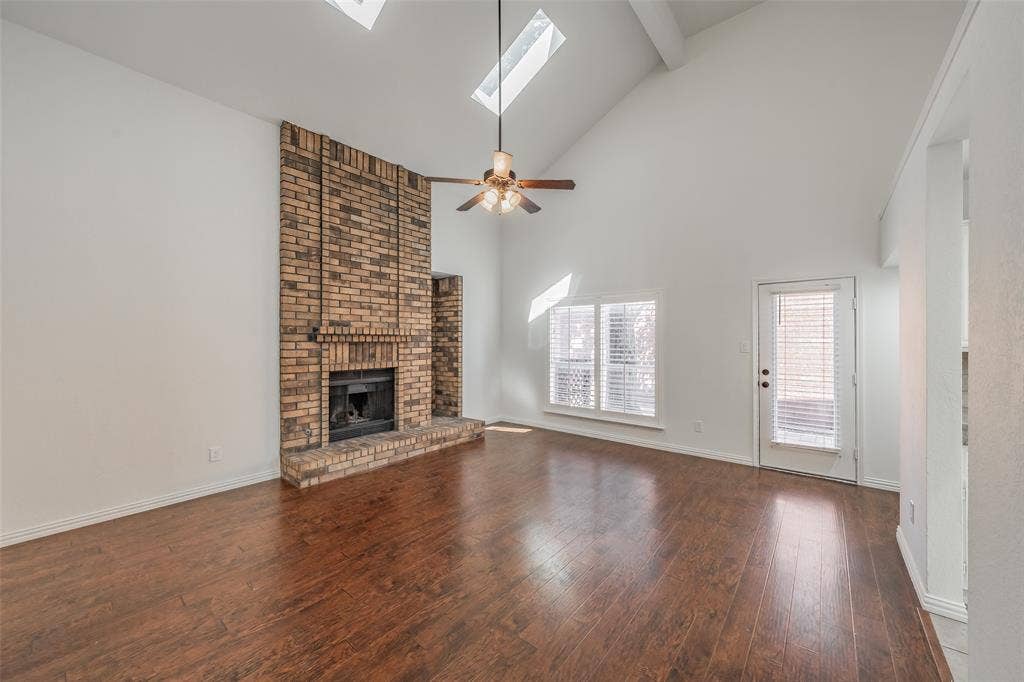 617 Dover Court, Coppell, TX 75019 Vaulted ceiling with exposed beam, wood flooring, brick fireplace, multiple skylights, and a ceiling fan in the living room