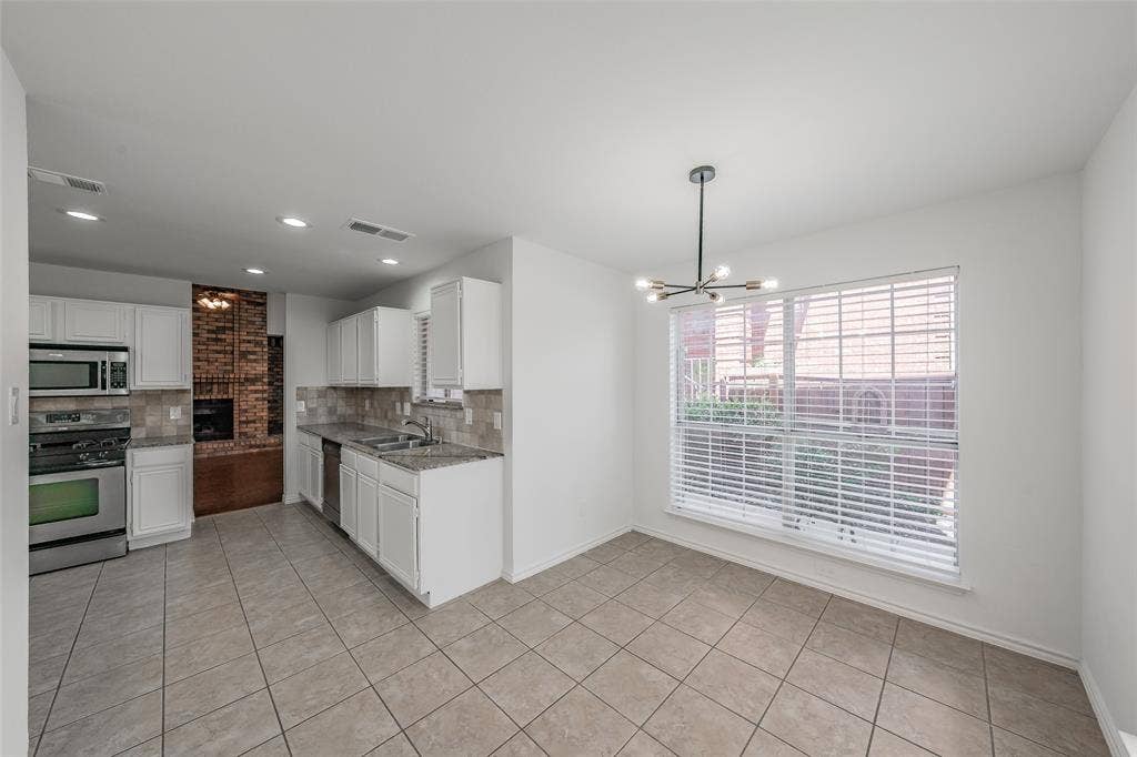 617 Dover Court, Coppell, TX 75019 Kitchen and dining area featuring tile flooring, white cabinetry, stainless steel appliances, and a modern chandelier