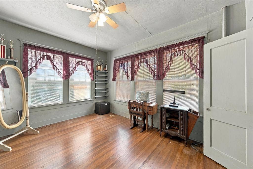 2725 Morrow Avenue, Waco, TX 76707 Spacious room featuring hardwood flooring, ceiling fan with light fixture, and multiple windows with burgundy swag valances