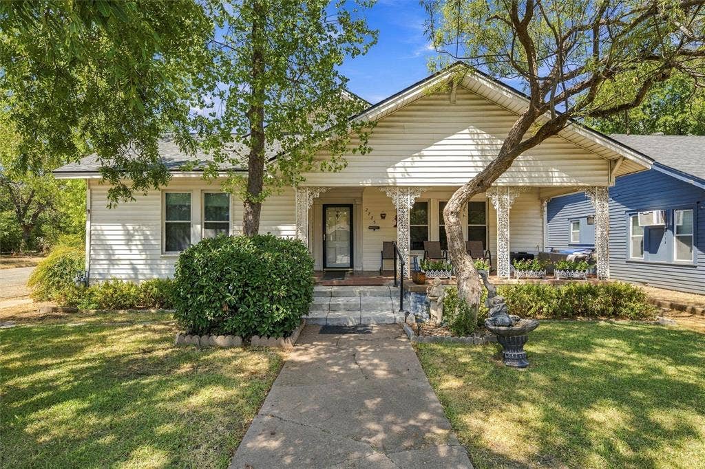 2725 Morrow Avenue, Waco, TX 76707 White siding exterior with a covered porch featuring decorative columns, a concrete pathway, and mature trees providing shade