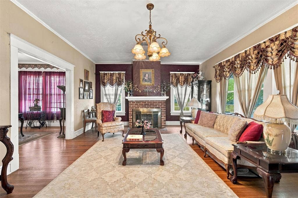2725 Morrow Avenue, Waco, TX 76707 Spacious room featuring wood-finish flooring, a brick fireplace with a detailed mantel, and a multi-arm chandelier
