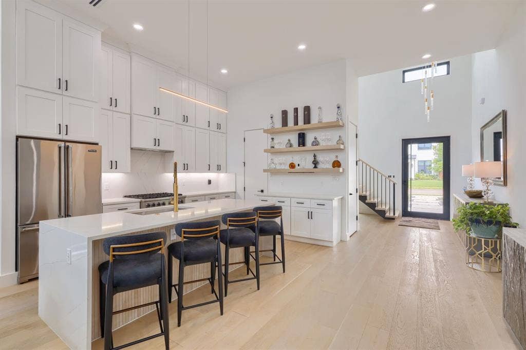 3950 Beechwood Lane, Dallas, TX 75220 Contemporary kitchen with an expansive island featuring seating, stainless steel appliances, white cabinetry, and wood-finish flooring