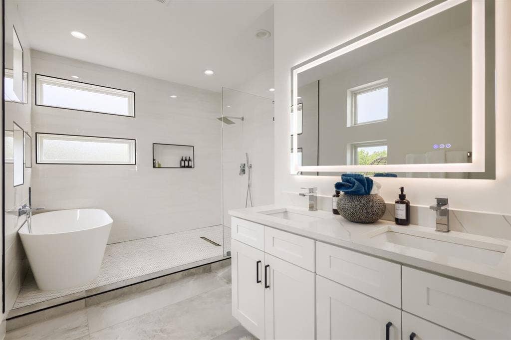 3950 Beechwood Lane, Dallas, TX 75220 Dual vanity with stone countertops and undermount sinks, illuminated mirror, freestanding soaking tub, glass-enclosed shower, and recessed wall niches